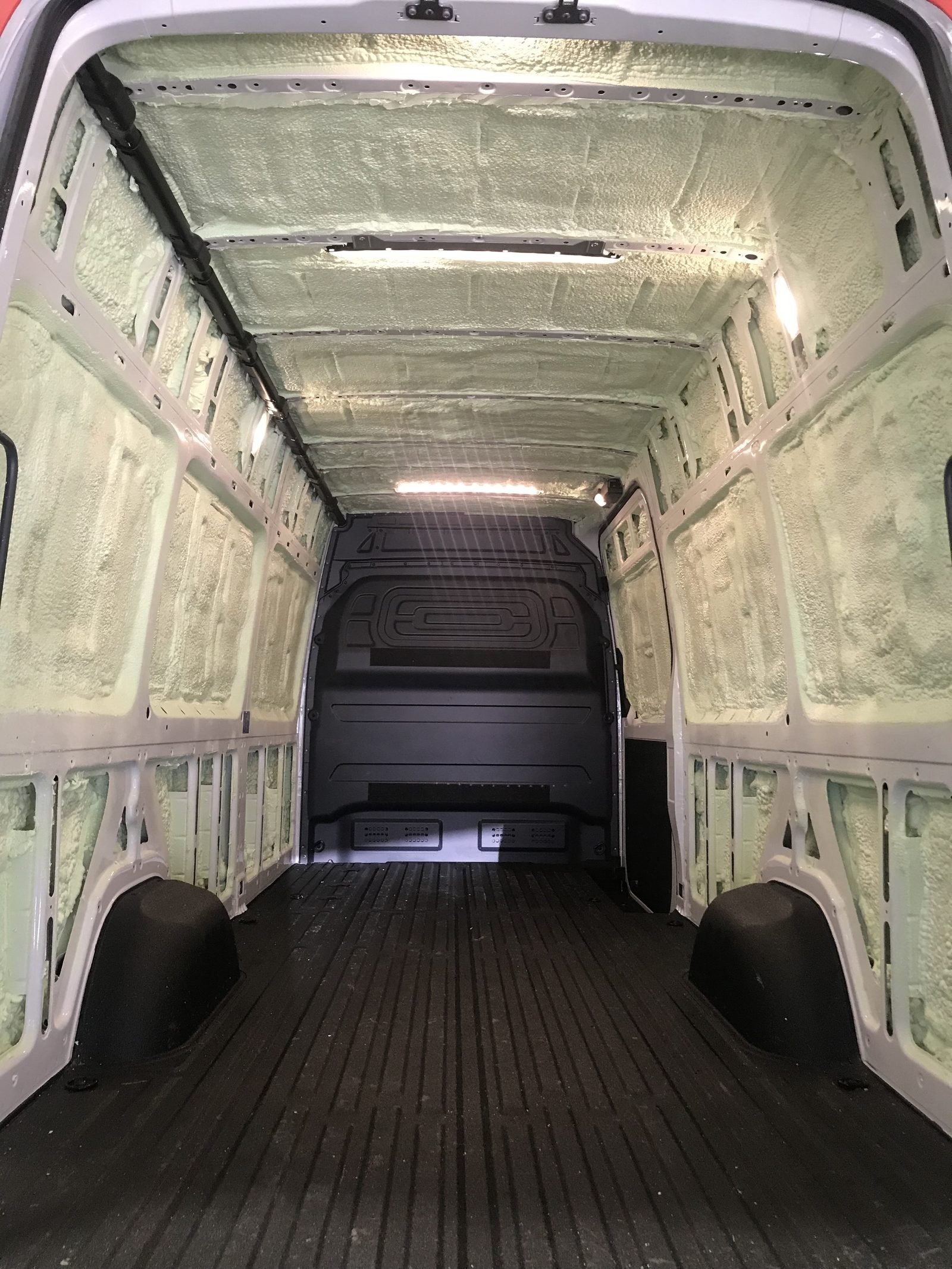 The inside of a cargo van sprayed with closed-cell polyurethane foam, filling the wall and roof ribs from the floor to the ceiling
